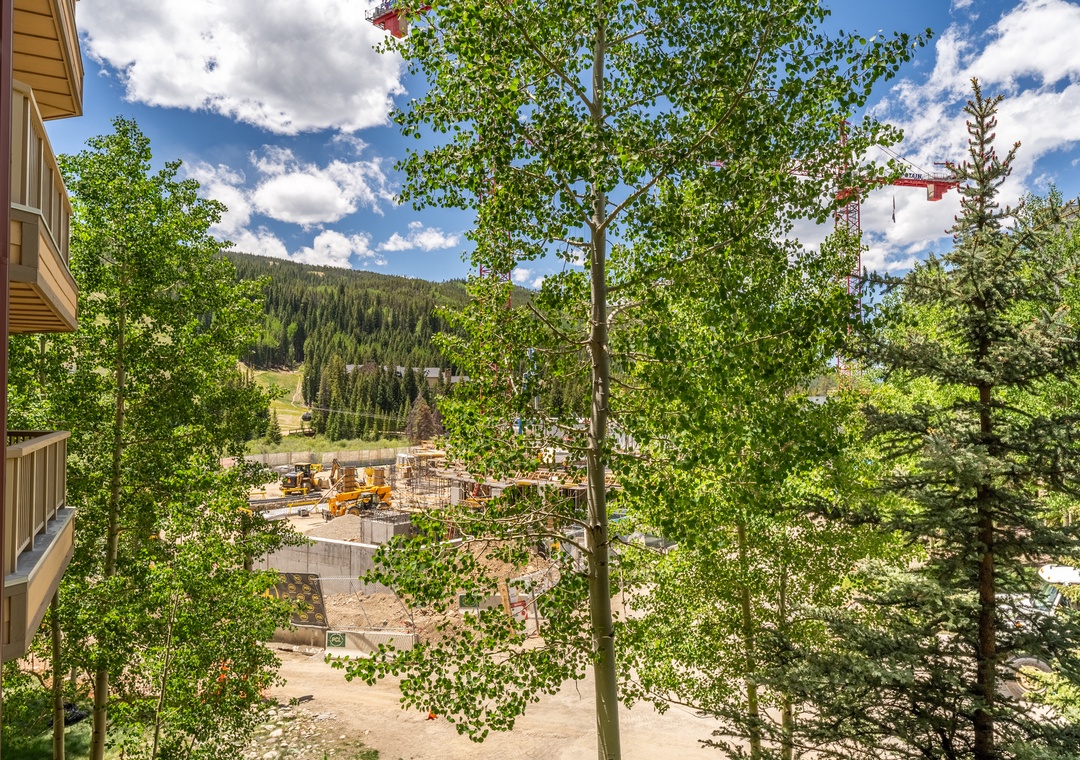 Mountain views and forested hillsides create a scenic backdrop with ongoing construction visible in the valley below.