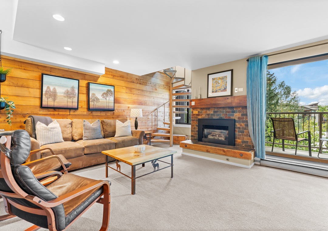 Relax in your spacious living area with warm wood accents, plush seating, and a cozy fireplace—perfect for unwinding after a day of adventure while enjoying natural light from the large windows.