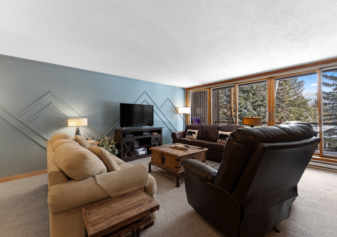 Settle into your cozy living room with plush seating and mountain views through floor-to-ceiling windows, perfect for relaxing after adventure-filled days.