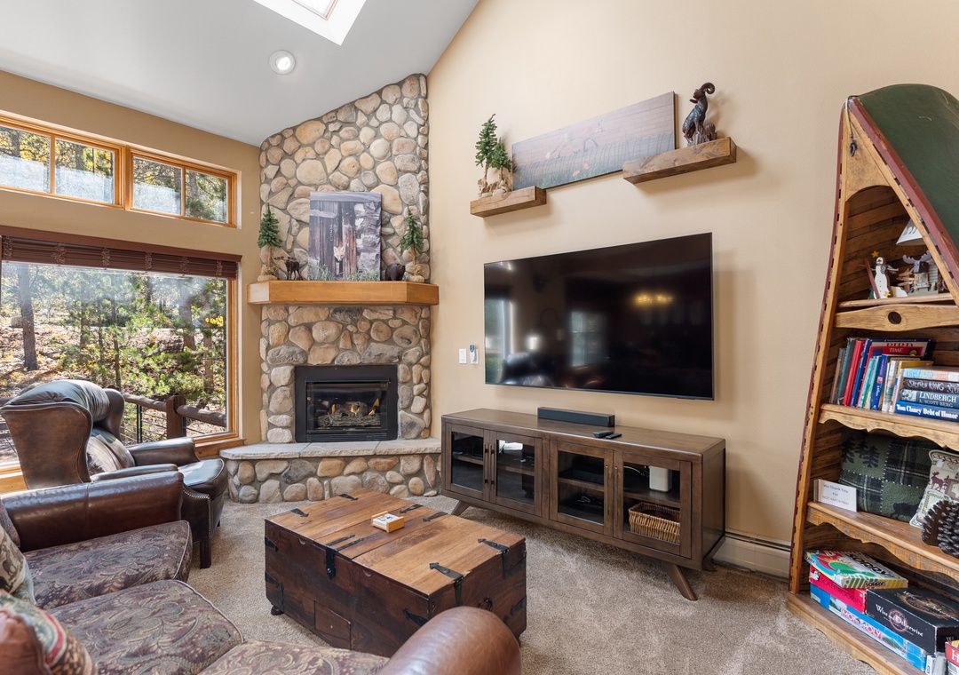 Curl up in this cozy living room featuring a stone fireplace, comfortable leather seating, and mountain views through large windows.