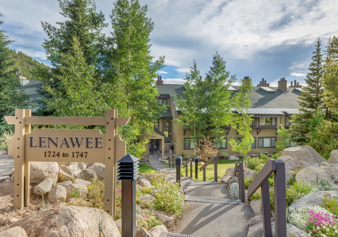 Lenawee entrance welcomes guests to mountain retreat surrounded by natural landscaping and towering evergreens.