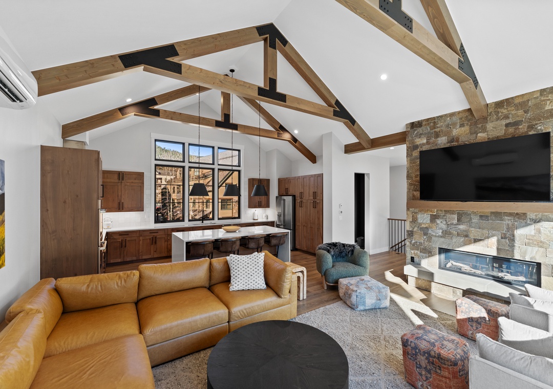 Relax in this stunning open-concept living space featuring soaring exposed beams, a cozy stone fireplace, and modern amenities for your perfect mountain getaway.