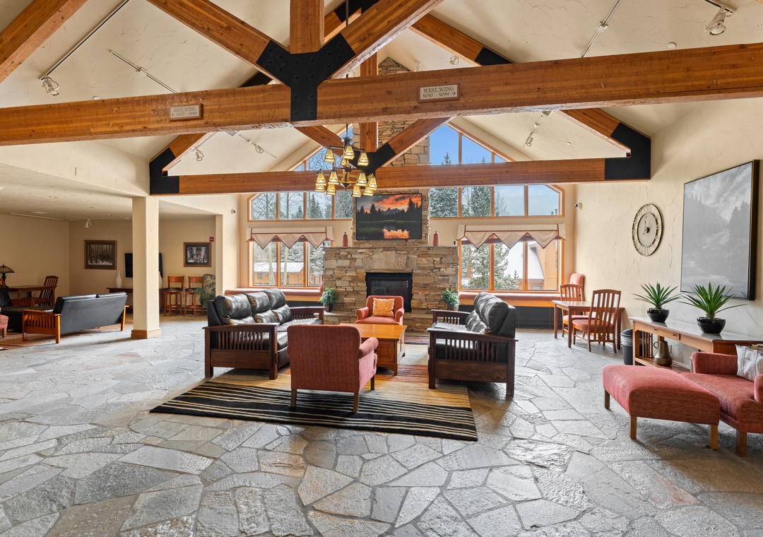 Unwind in this stunning great room with soaring timber beams, a cozy stone fireplace, and natural light pouring through expansive windows—your perfect mountain retreat awaits.