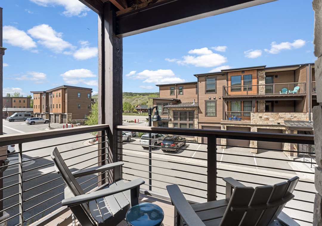 A covered balcony overlooks a modern mountain neighborhood, offering a quiet spot to relax with morning coffee while taking in views of surrounding homes and hillsides.