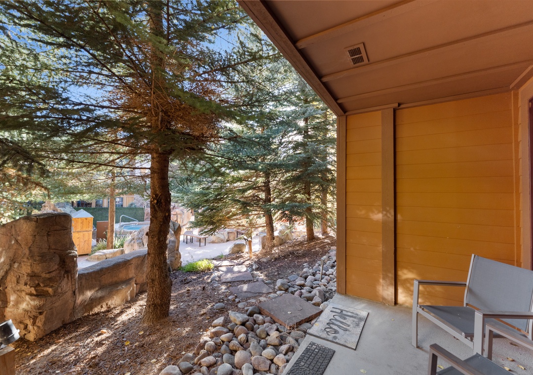 Step onto your private covered patio where modern seating awaits beneath towering pines and natural stone accents.