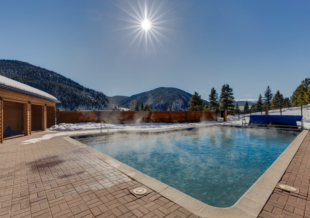 Heated outdoor pool surrounded by snow-capped mountains and bright winter sun creates the perfect alpine retreat setting.