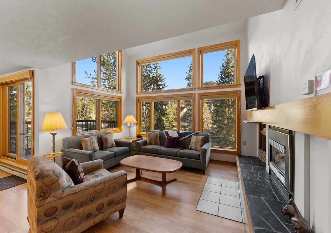 Relax in your bright living room with soaring windows framing forest views, cozy fireplace, and comfortable seating for memorable evenings together.