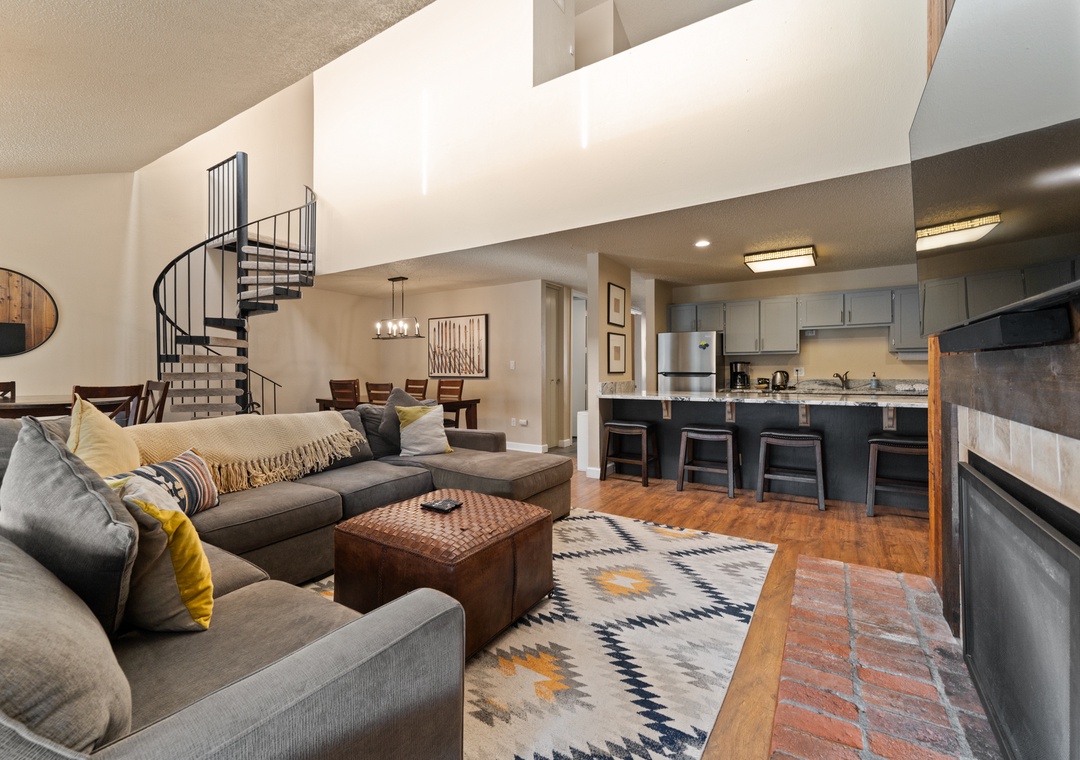 Relax on the plush sectional in your open-concept space featuring a stunning spiral staircase and gourmet kitchen with breakfast bar.