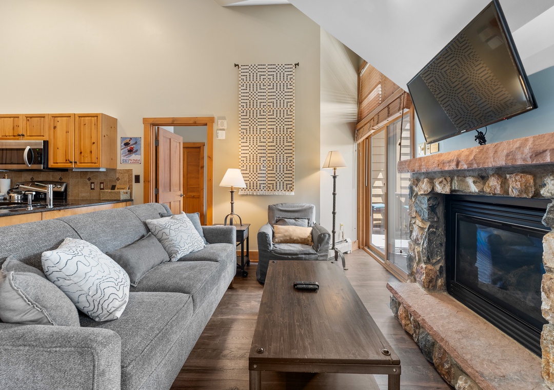 Cozy up on the plush sectional sofa by your stone fireplace, perfect for relaxing after mountain adventures with kitchen convenience nearby.