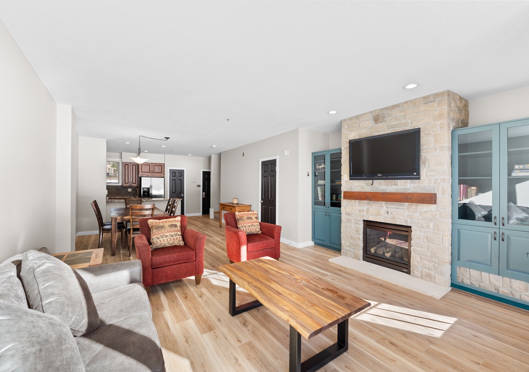 Relax in your spacious open-concept living area featuring warm hardwood floors, a cozy stone fireplace, and stylish furnishings perfect for unwinding.
