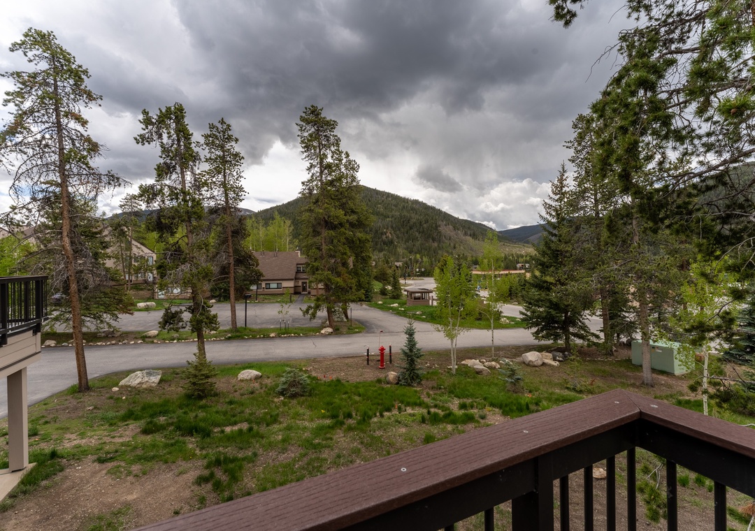 Mountain views stretch beyond your deck, showcasing forested peaks and the peaceful neighborhood below amid dramatic cloudy skies.