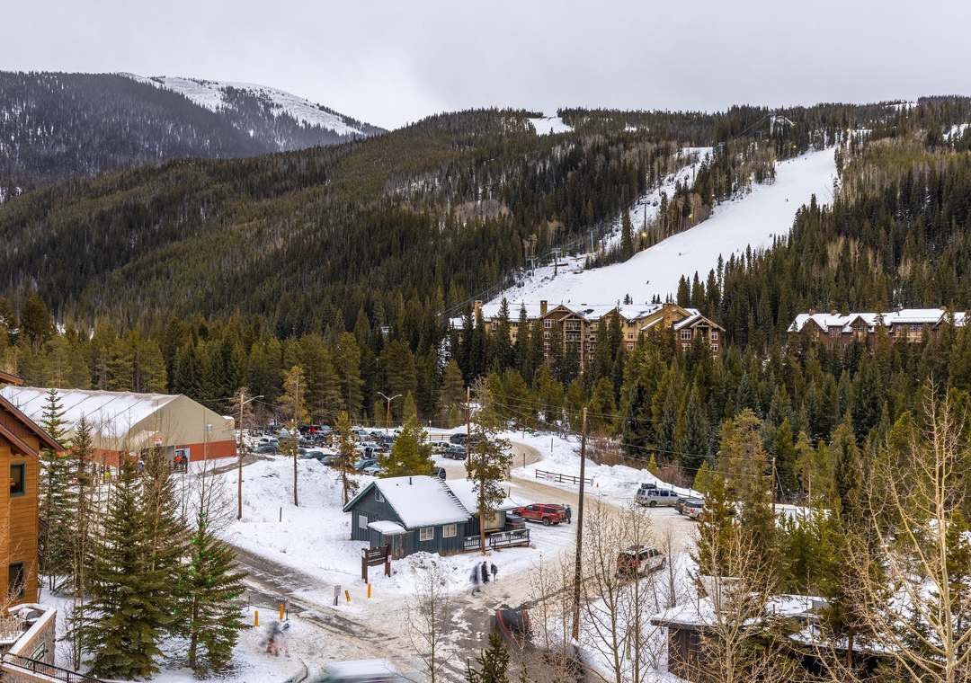 Snow-covered ski slopes and mountain village create a perfect winter resort setting surrounded by dense evergreen forests.