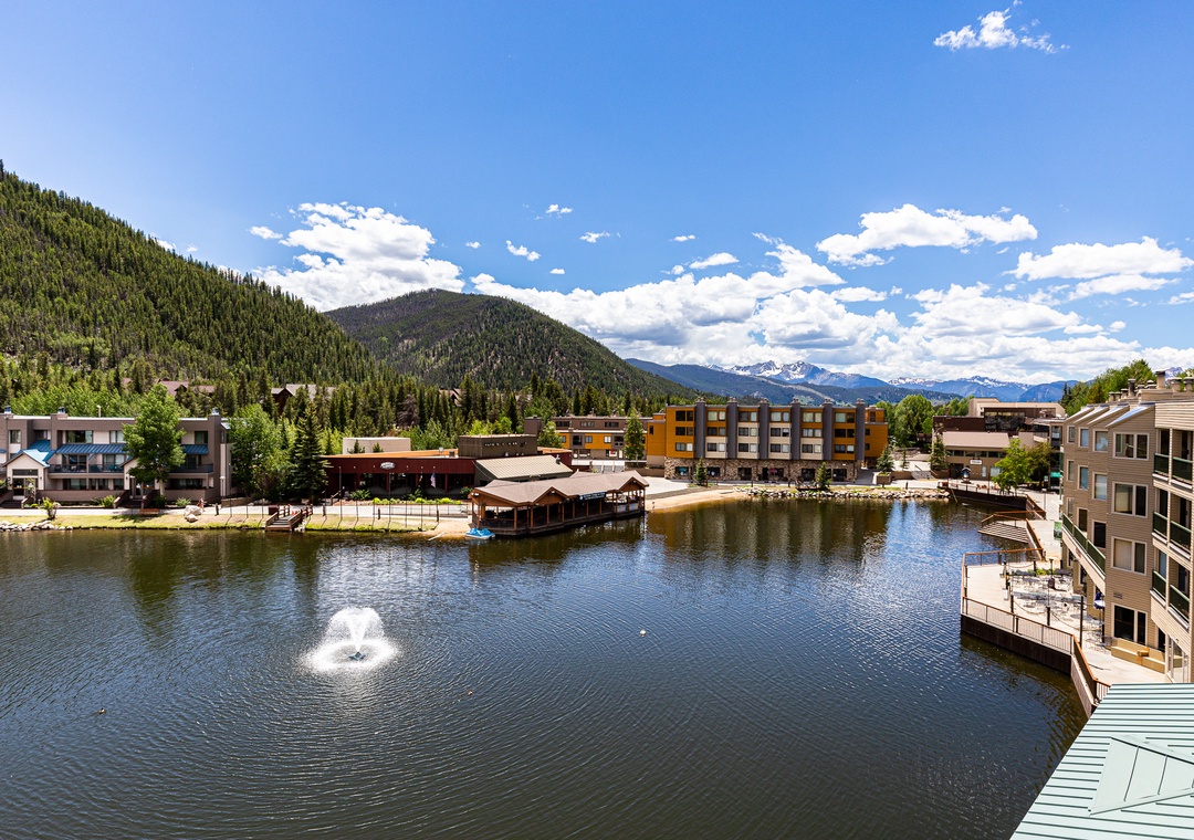 Mountain resort town featuring lakefront buildings, forested peaks, and scenic alpine surroundings with clear blue skies.