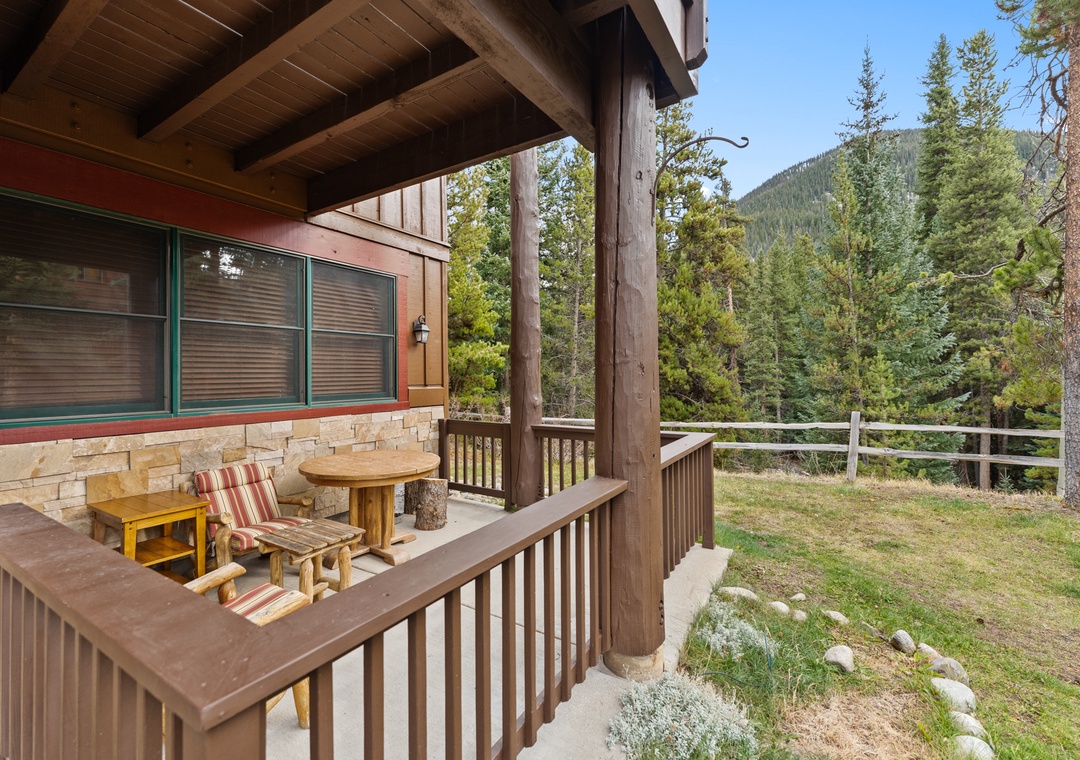 A covered deck with rustic charm features wooden seating perfect for morning coffee while taking in the forested mountain backdrop.