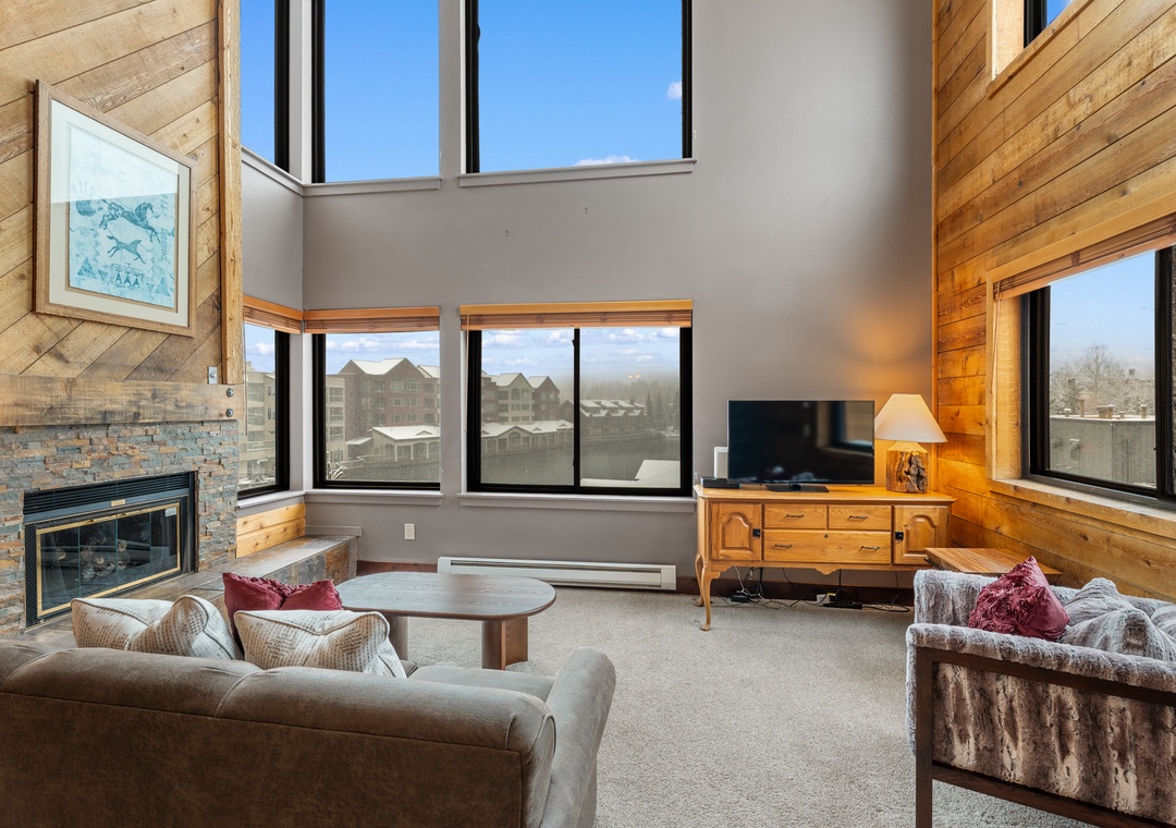 Unwind in your vaulted living room with soaring windows framing mountain views, a cozy stone fireplace, and warm wood accents inviting you to settle in after a day of adventure.