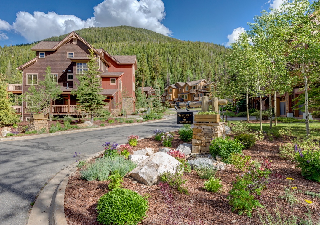 Mountain resort entrance with landscaped grounds and forest-covered peaks rising behind upscale vacation homes.