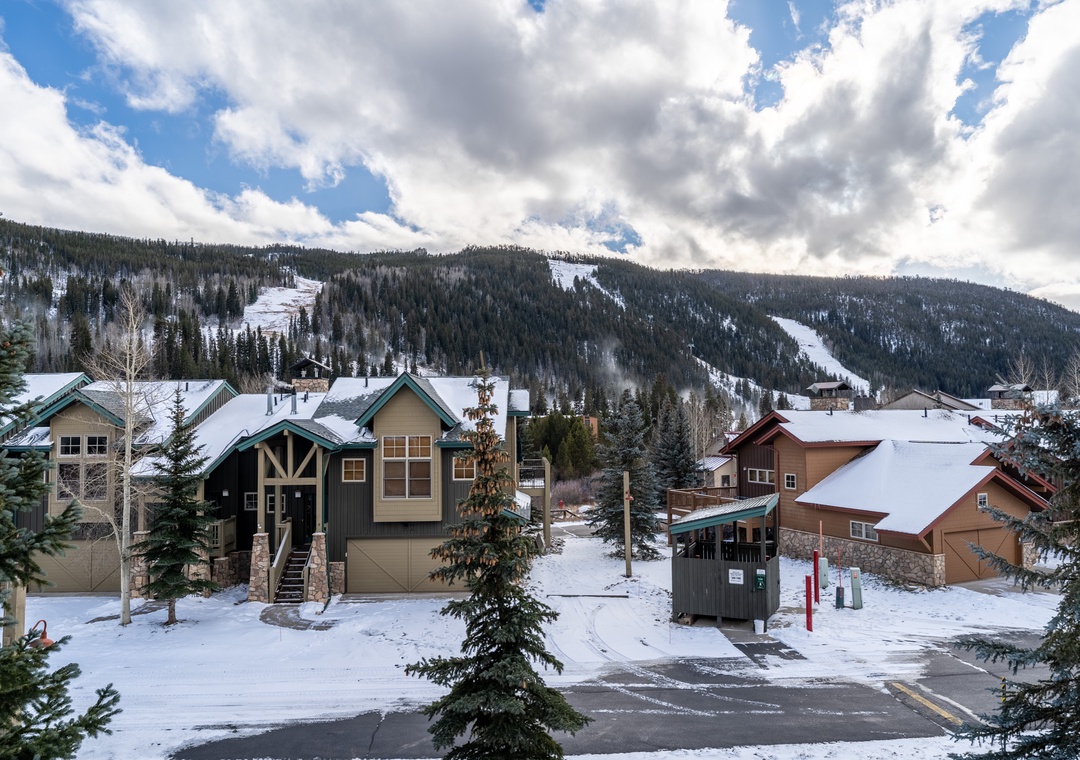 Charming mountain village nestled beneath snow-covered slopes with ski runs visible on the forested hillsides.