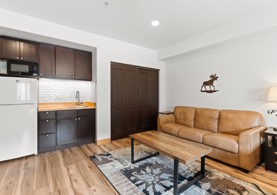 Unwind in your open-concept living area with a leather sofa, modern kitchenette, and warm wood tones creating a welcoming mountain retreat vibe.