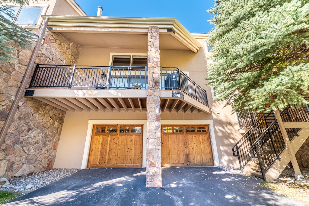 Two-story vacation rental featuring stone accents, wooden garage doors, and covered balcony surrounded by mature trees.