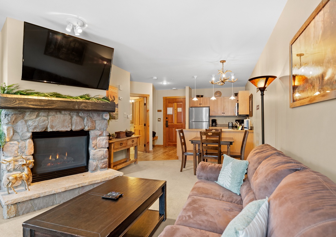 Unwind in your cozy living space with a crackling stone fireplace, plush sofa, and open kitchen perfect for memorable mountain evenings.