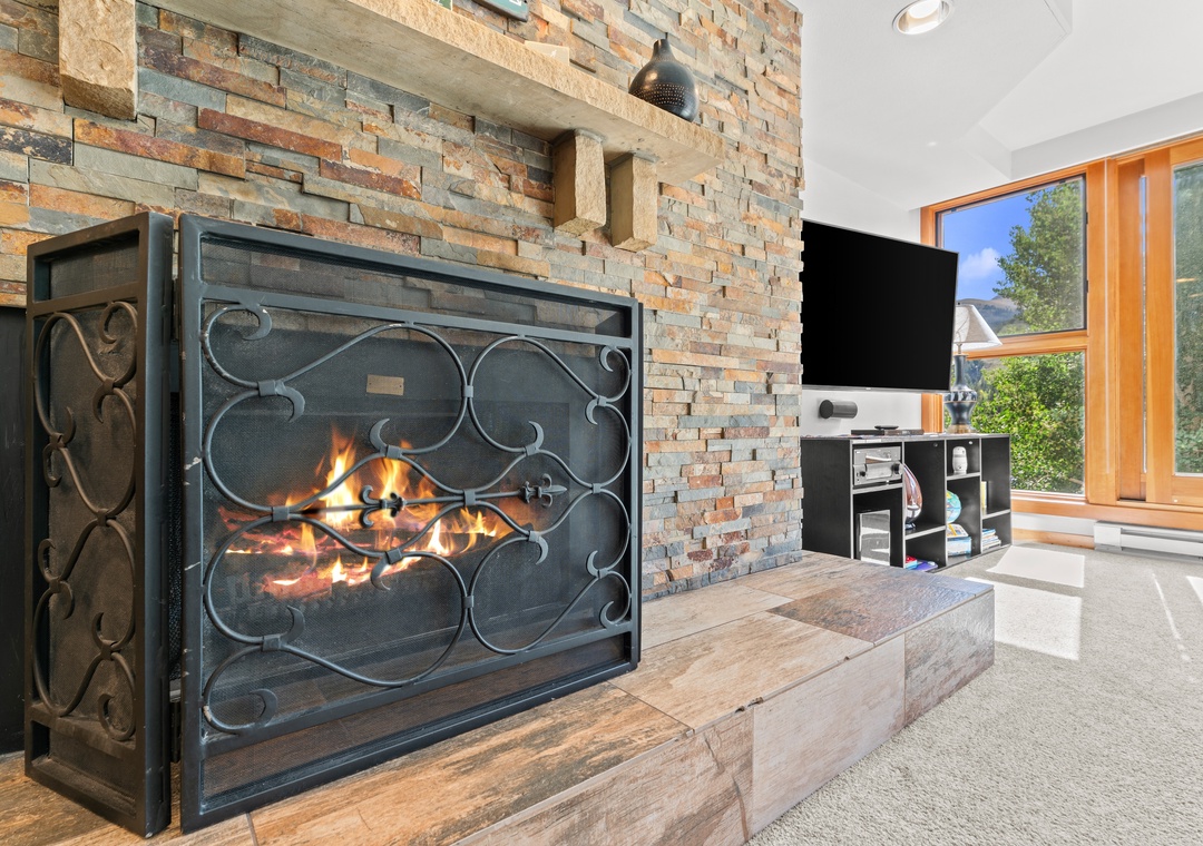 Gather around the warmth of a crackling fireplace framed by stunning stone accent walls. Large windows frame lush greenery outside, filling your living space with natural light.