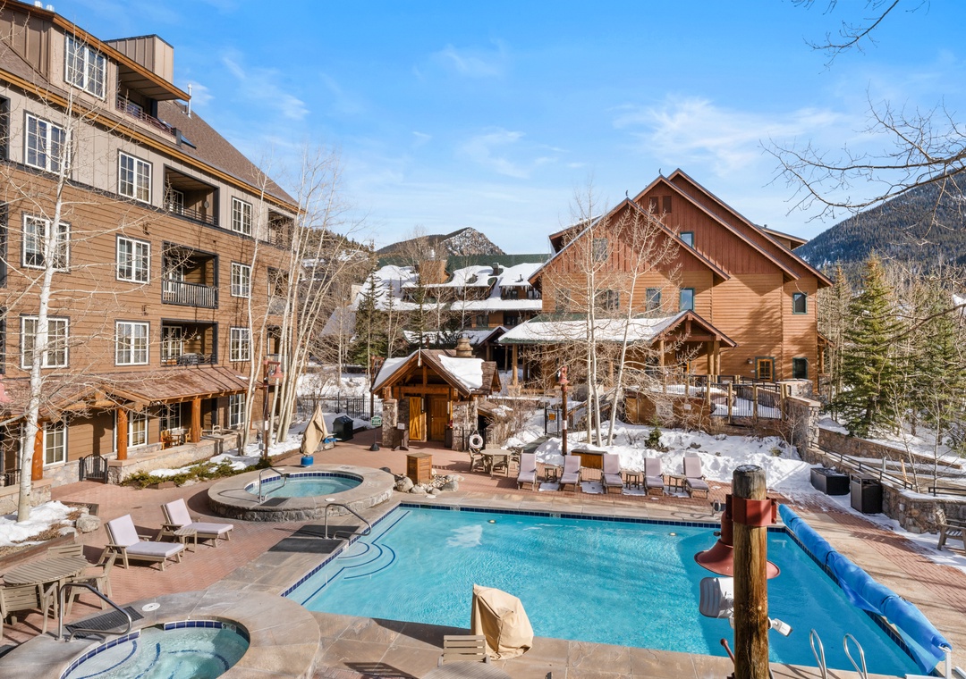 Mountain resort property featuring outdoor pools and hot tubs surrounded by snow-covered buildings and scenic alpine views.