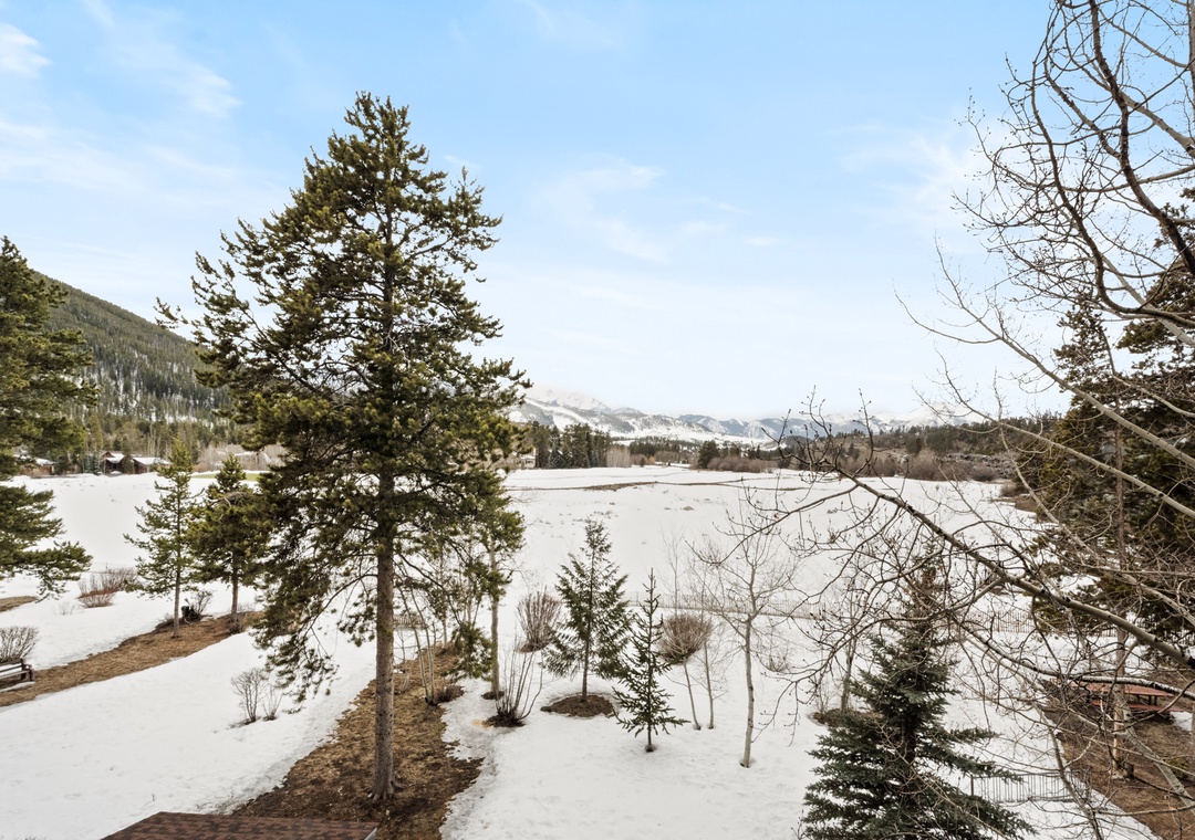 A serene mountain retreat nestled in a winter landscape, where snow-dusted grounds meet towering evergreens and distant peaks create a peaceful alpine backdrop.