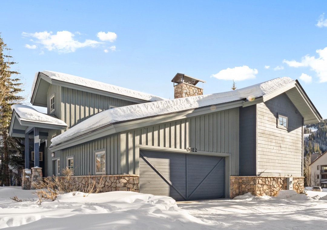 Modern mountain home with stone and cedar siding, featuring a heated garage and scenic alpine backdrop.