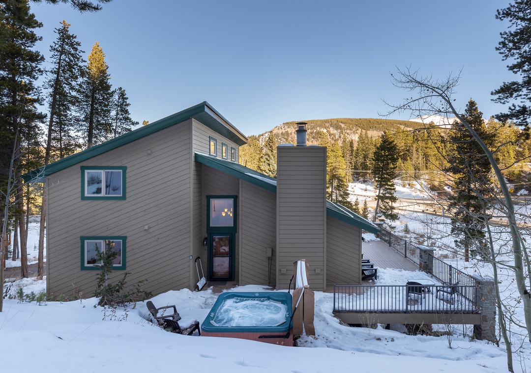 Modern mountain retreat with private hot tub surrounded by snow-covered peaks and towering evergreens.