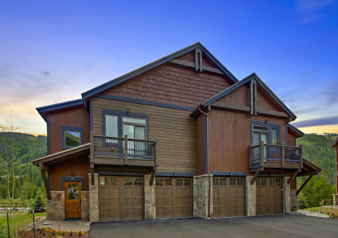 Mountain lodge duplex with stone and wood architecture nestled among forested hills at twilight.