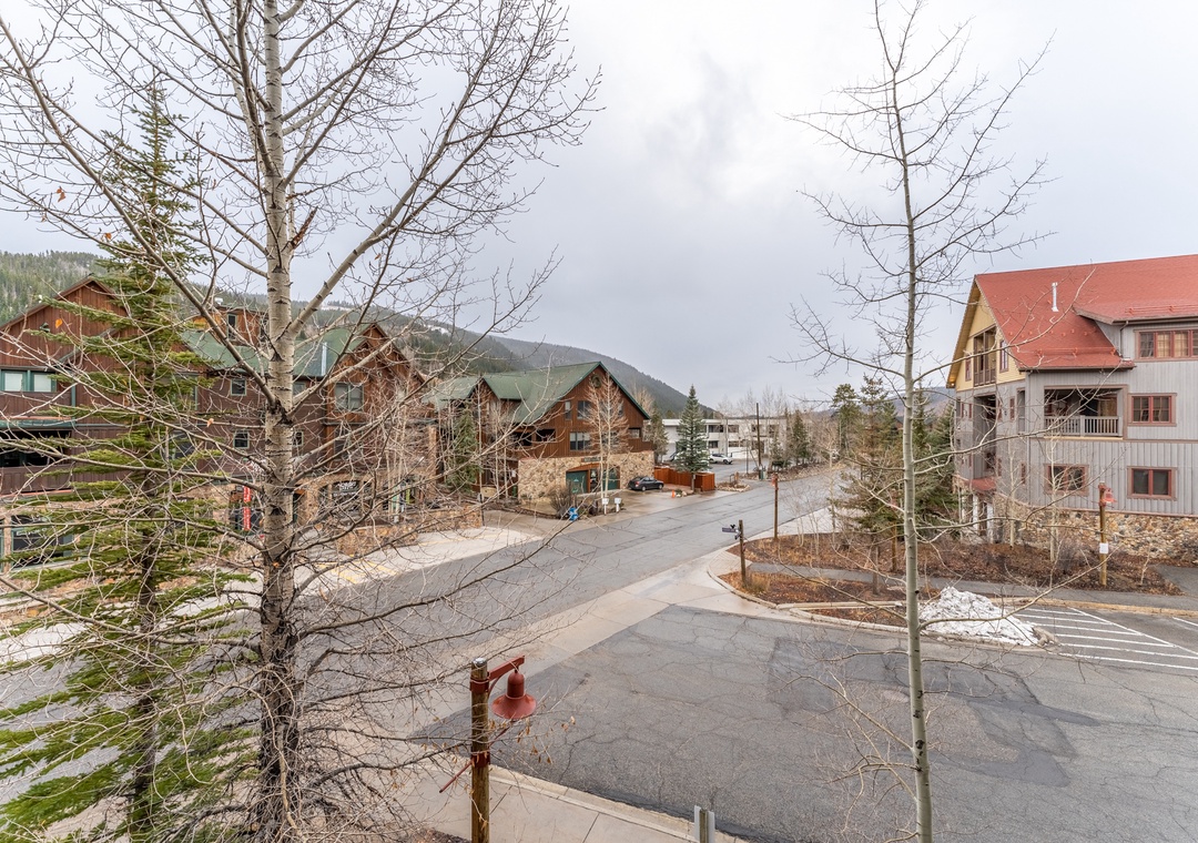 Quiet mountain village street with alpine chalets and forest-covered hills creating a peaceful arrival setting.