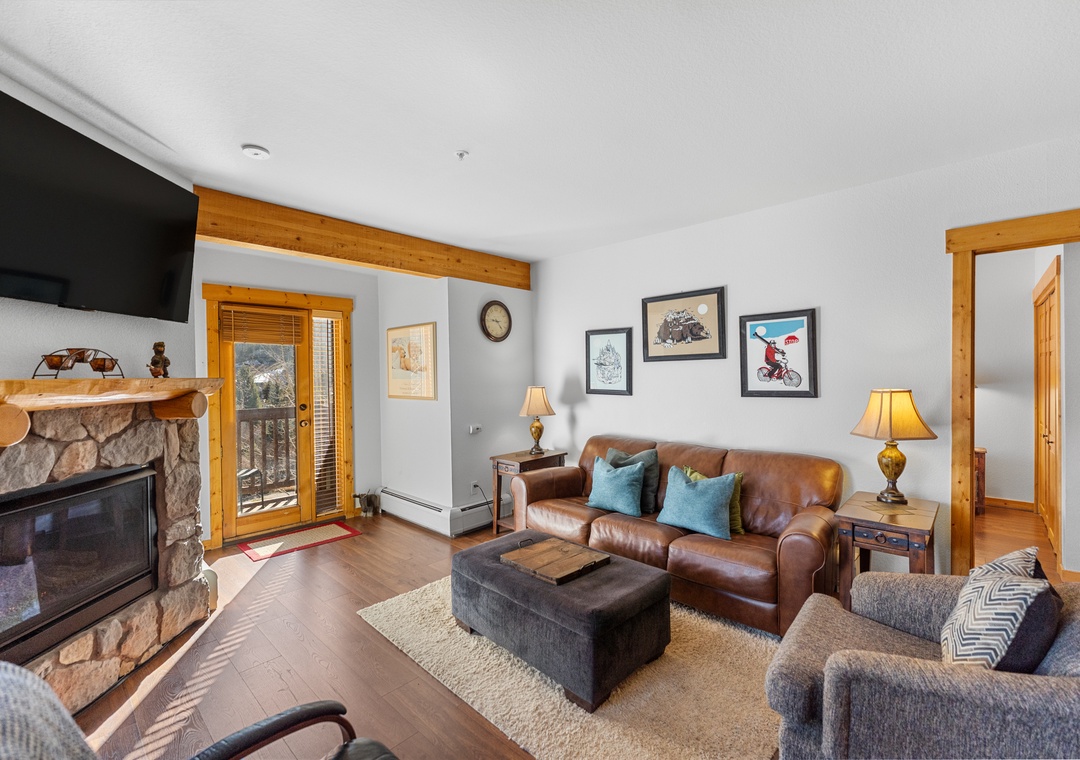 Cozy up in this warm living room with a stone fireplace, leather sofa, and mountain views from your private balcony.