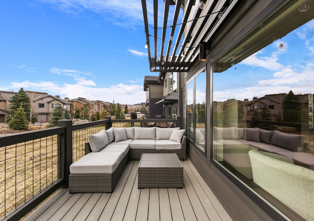 Unwind on your private deck with comfortable sectional seating, offering peaceful neighborhood views and seamless indoor-outdoor living through sliding glass doors.