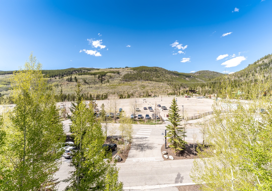 Mountain valley parking area surrounded by forested hills and spring foliage under clear blue skies.