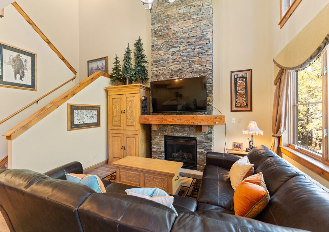 Cozy up in your mountain retreat's living room, where stone fireplace warmth meets leather comfort beneath soaring ceilings.