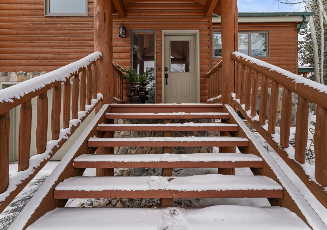 Snow-dusted wooden steps lead to the welcoming entrance of this charming log cabin retreat.