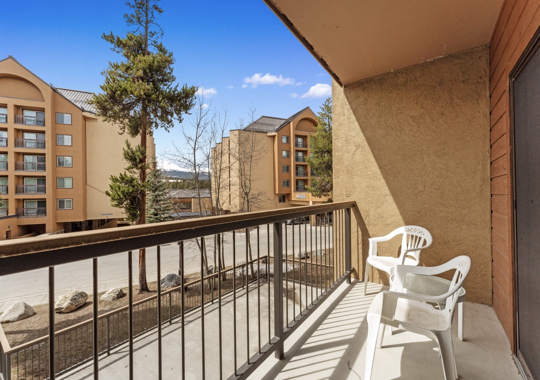 A private balcony with outdoor seating overlooks neighboring buildings and natural surroundings, offering a peaceful spot to enjoy the mountain resort atmosphere.