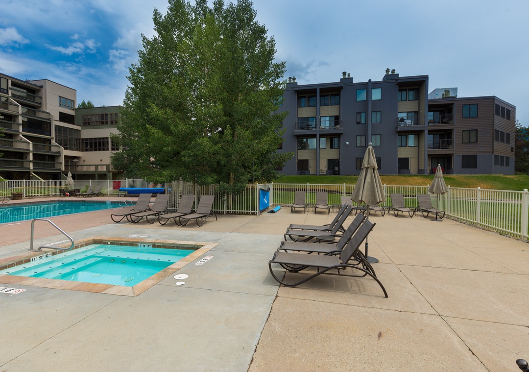 Modern apartment complex with outdoor swimming pool and hot tub area surrounded by contemporary residential buildings.