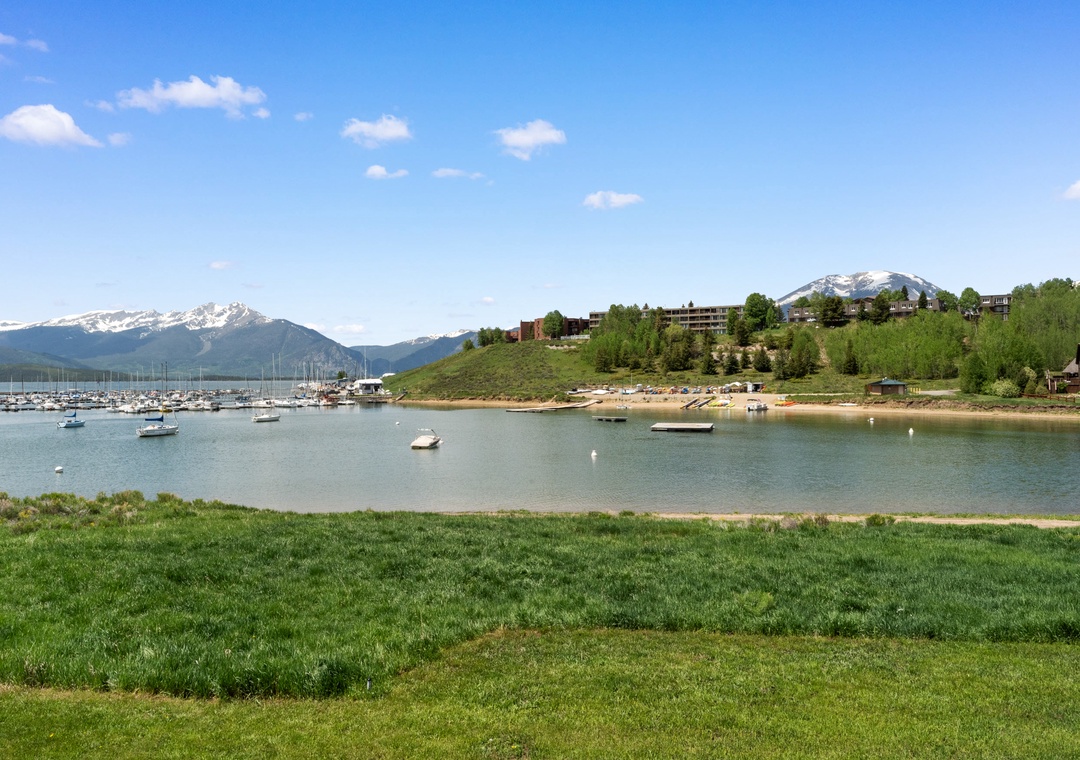 Peaceful lakefront setting with marina, mountain backdrop, and residential buildings nestled among green hills.