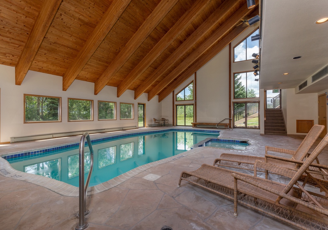 Your private indoor pool awaits beneath soaring wood beams, with lounge chairs positioned perfectly for relaxation and garden views through expansive windows.