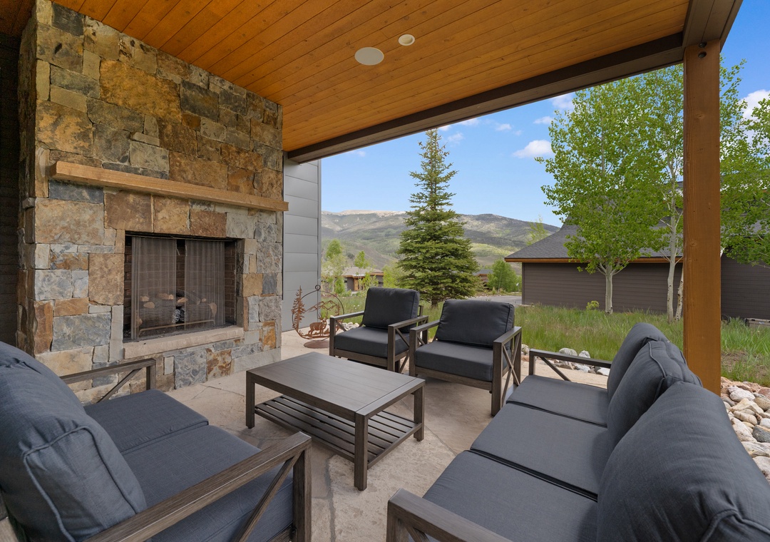 Covered patio with an outdoor fireplace framed by mountain views. The seating area offers a perfect spot to unwind while taking in the natural beauty of the surrounding landscape.