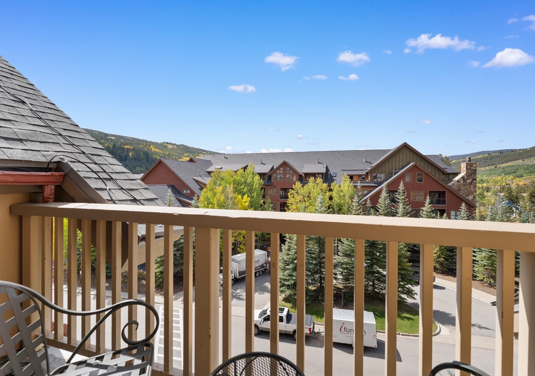 Mountain resort balcony overlooking scenic village and forested hills with autumn foliage under clear blue skies.