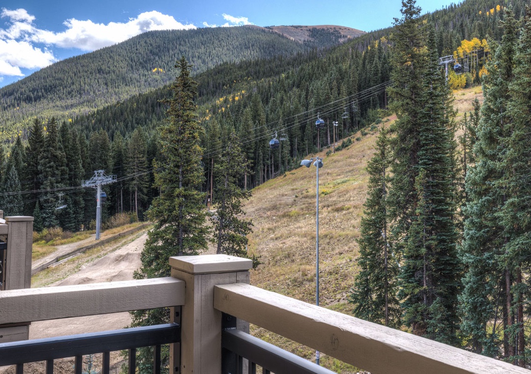 Mountain vista stretches beyond the ski area, showcasing forested slopes and autumn colors during bright daylight hours.