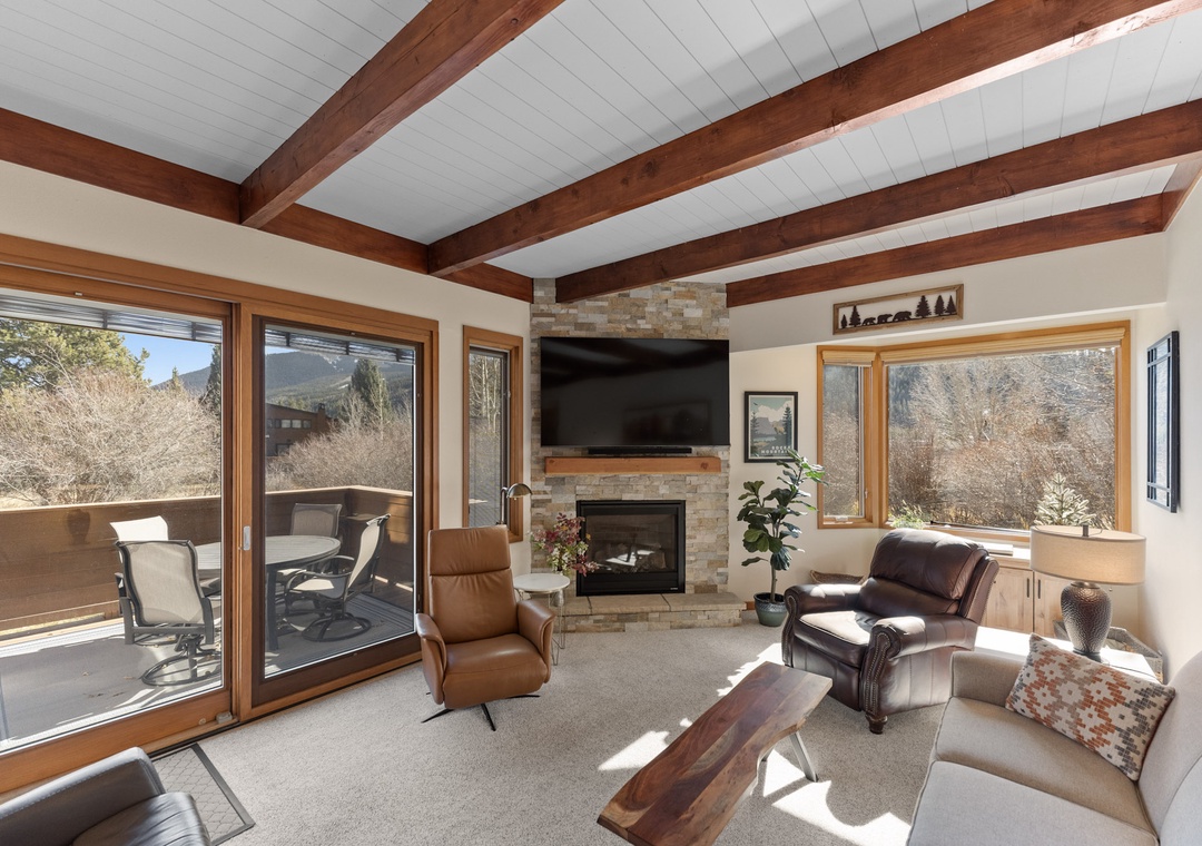 Cozy up in your sunlit living room where exposed beams meet mountain views, complete with fireplace warmth and patio access.