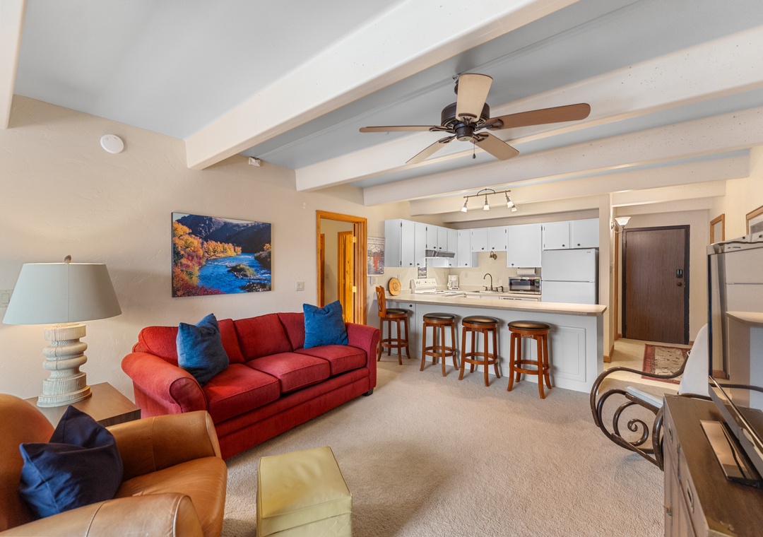 Relax in your open-concept space with exposed beams, red sofa, and fully equipped kitchen with breakfast bar seating.