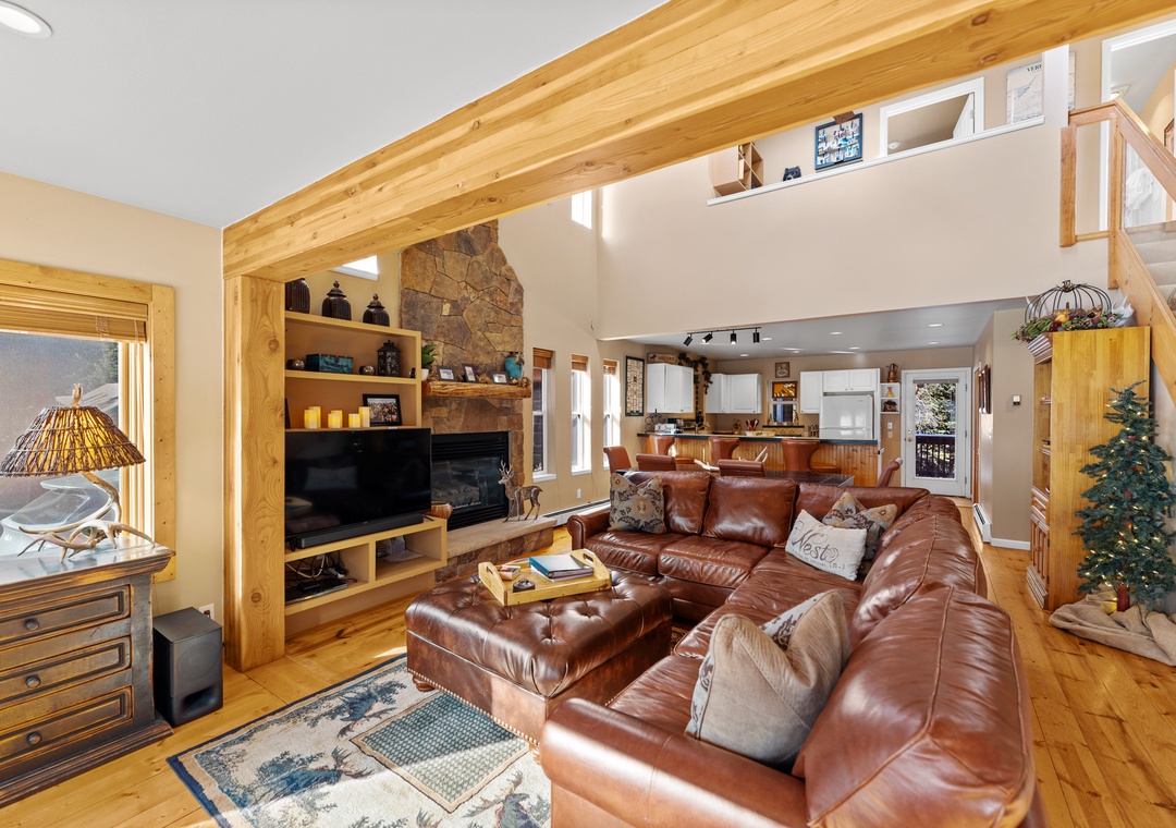 Relax in your spacious living room with rich leather seating, stone fireplace, and exposed wood beams creating mountain cabin charm.
