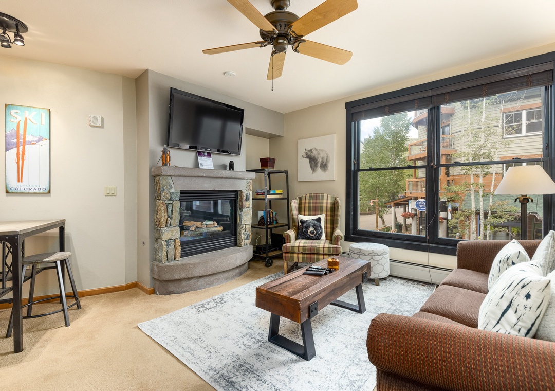 Cozy up in your stylish living room with a stone fireplace, plush seating, and warm mountain views through expansive windows.