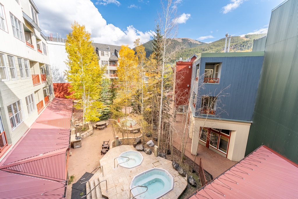 Stunning mountain resort courtyard with hot tub and seasonal autumn foliage framed by forested peaks.