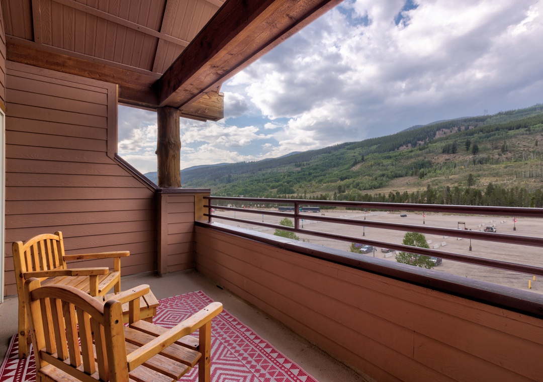 Unwind on your private balcony with stunning mountain views, where comfortable wooden chairs invite peaceful moments overlooking the scenic landscape below.