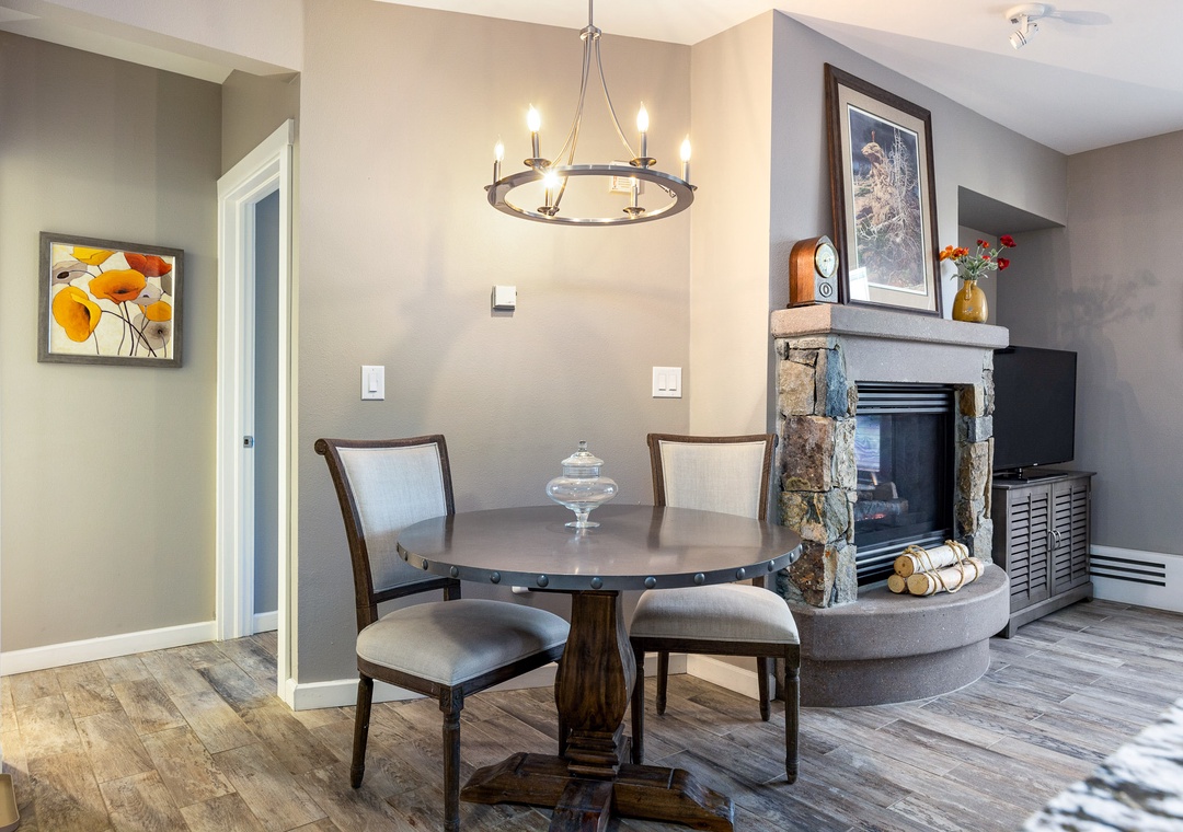 Gather around your intimate dining table beneath elegant chandelier light, with a cozy stone fireplace creating the perfect ambiance for memorable meals.